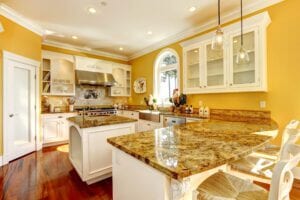 A photo of a kitchen with yellow walls and yellow and brown marbled countertops with white cabinets.