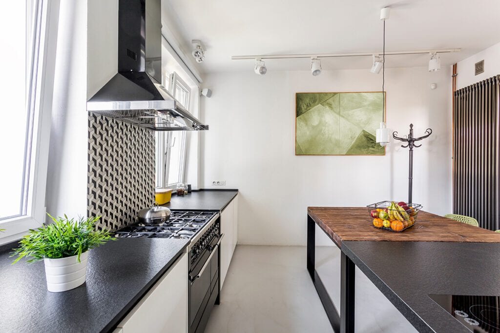 a modern-style kitchen with black countertops, a gas range oven, a reclaimed wood table, and a modern green painting