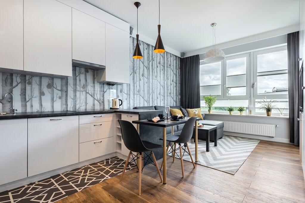 A kitchen with modern white cabinets contrasted by gray forest wallpaper.