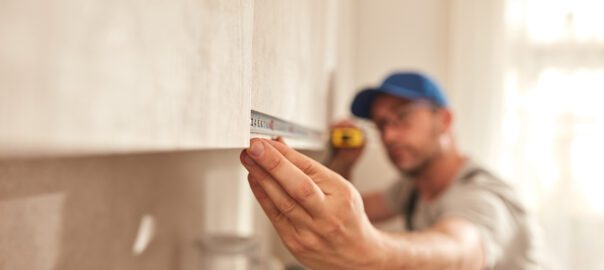 Handyman measuring a kitchen cabinet with a tape measure, focusing on precise alignment during installation.