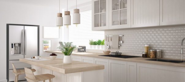 A kitchen with white, modern cabinetry and an island with three hanging lights over it.